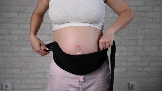A pregnant woman removes a two-piece black bandage. Cropped belly.
