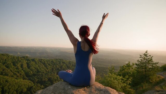 Sports Girl Meditates During Sunrise. Athletic Woman Exercising in the Mountains, Sitting in Lotus Yoga Position. Healthy Lifestyle and Wellbeing, Zenism Concept. Slow Motion.