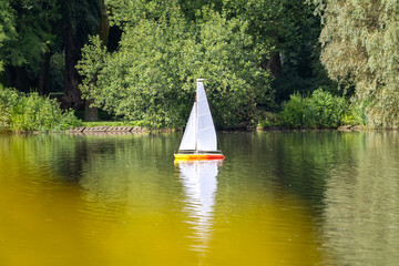 Remote control colorful sailboat sailing farm back in a calm lake.