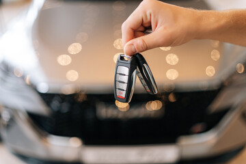 Close-up cropped shot of unrecognizable customer male holding in hand car key from new auto after buying in dealership office on blurred background of new auto. Concept of choosing new car