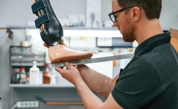 Standing, checking measure of the prosthesis. Technician working in modern laboratory