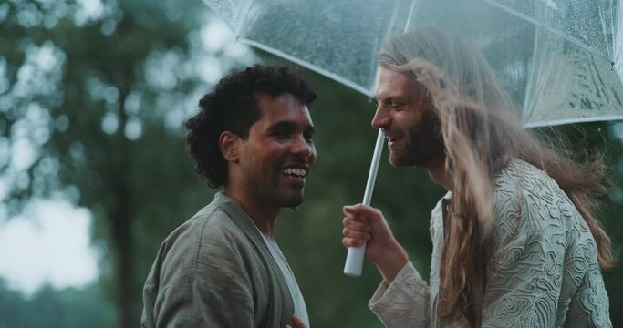 Young queer couple laughing under an umbrella. 