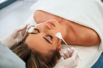 Naklejka premium Brushes are used to clean skin. Woman face getting facial care by beautician hands at spa salon