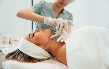 Yellow colored syringe, making injection. Woman face getting facial care by beautician hands at spa salon