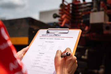 A mechanical engineer is inspecting the condition of truck crane vehicle (as blurred background) before start the operation on the inspection checklist form. Industrial working with safety practice.