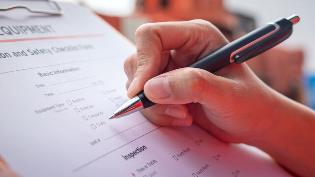 A mechanical engineer is inspecting the condition of truck crane vehicle (as blurred background) before start the operation on the inspection checklist form. Industrial working with safety practice.