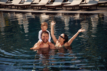 In the water. Happy family of father, mother and son are in the pool