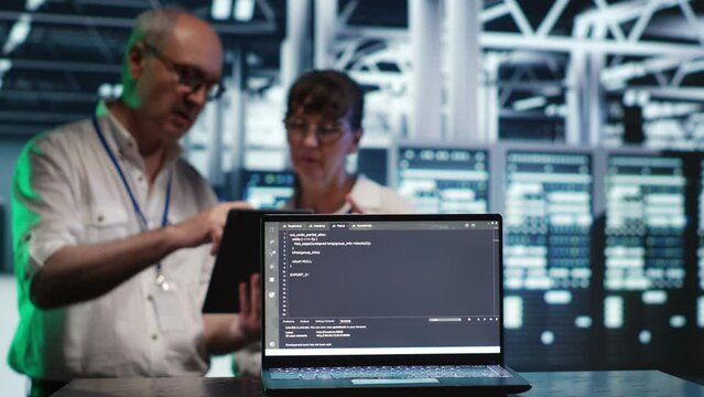 Octogenarian managers in data center, solving tasks on tablet while running scripts on laptop terminal. Adept supervisors amidst servers, accessing databases and manipulating lines of code