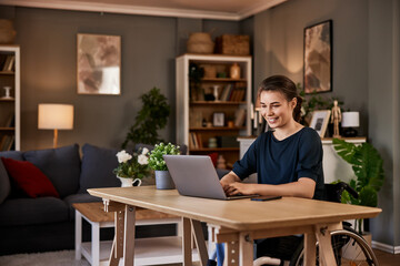 Cheerful woman in a wheelchair working on laptop at home office.