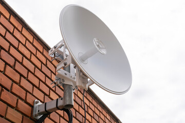 White satellite dish in front of brown brick wall