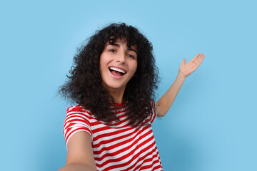 Beautiful young woman taking selfie on light blue background