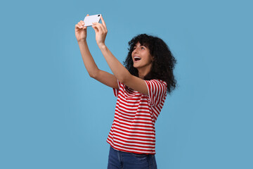 Beautiful young woman taking selfie on light blue background