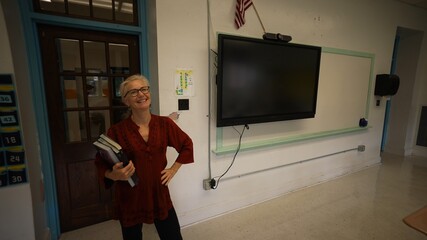 Portrait of smiling happy teacher entering an empty classroom, turning lights, on optimistic about the future of education. US American flag and smart board in room.