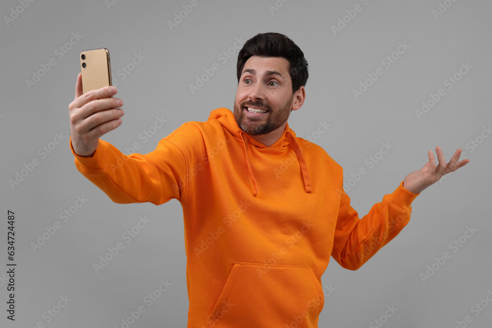 Wall mural Puzzled man taking selfie with smartphone on grey background