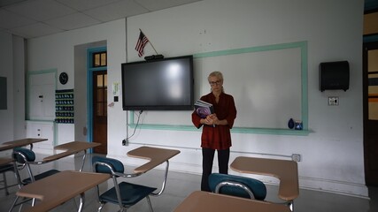 Sad unhappy teacher in an empty classroom with the lights turned off during budget cuts or a...
