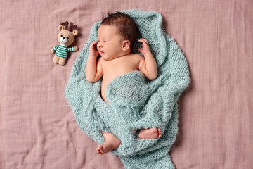 Cute newborn baby with toy deer in turquoise knitted blanket lying on bed, top view