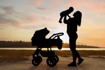 Mother with baby walking outdoors at sunset, silhouette