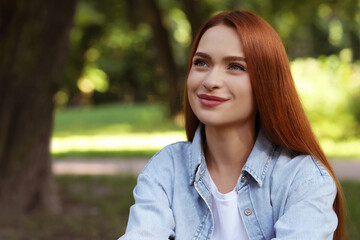 Fototapeta premium Portrait of beautiful young woman with red hair outdoors. Space for text. Attractive lady posing for camera