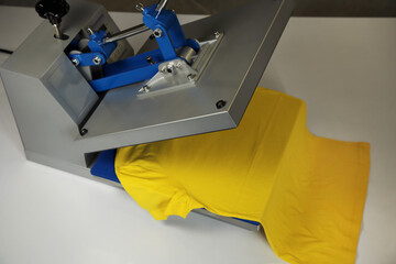 Printing logo. Heat press with yellow t-shirt on white table