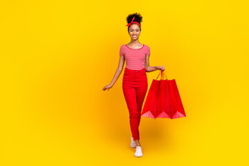 Full size photo of funky young girl walk hold shopping bags dressed stylish red striped clothes isolated on yellow color background