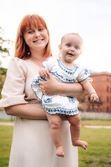 Happy smiling mom with a cute baby in park. A young woman is holding a child. Motherhood