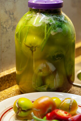 Glass jars with green tomatoes stand on the table....