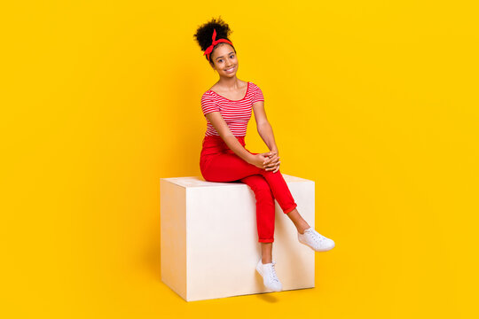 Full length photo of sweet adorable girl dressed red striped t-shirt sitting white platform isolated yellow color background