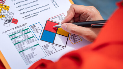 A safety engineer is using pen to rating the health risk assessment level of chemical hazardous material in the paperwork form. Industrial safety working scene, close-up and selecitve focus.