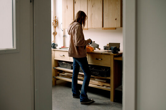 Female teenage student cutting wood during carpentry class seen through doorway