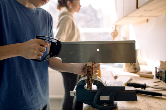 Midsection of male teenage student cutting wood with saw in carpentry class