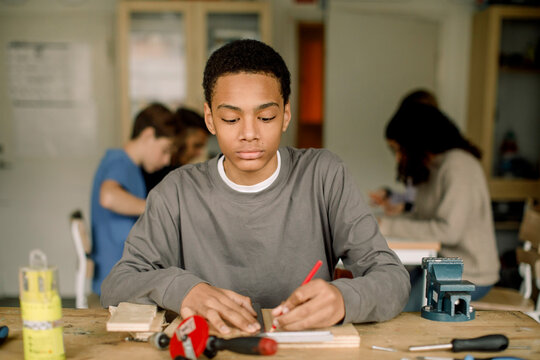 Focused male teenage student measuring wood during carpentry class at high school
