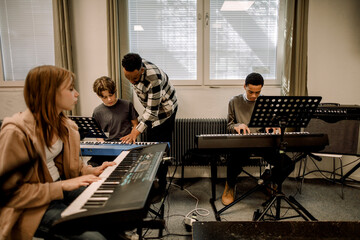 Teacher assisting teenage students during piano class at high school