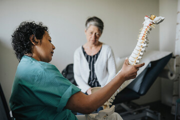 Doctor explaining senior patient over spine model in clinic