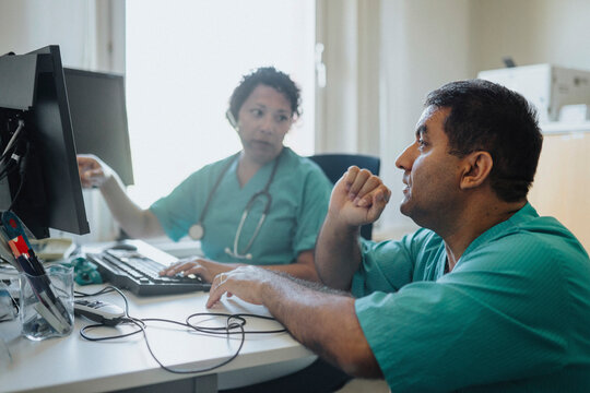 Male and female doctors discussing over computer at desk in hospital