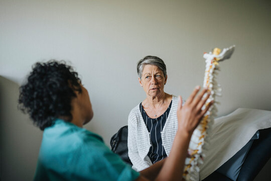 Multiracial doctor and patient discussing over spine model in clinic - Powered by Adobe