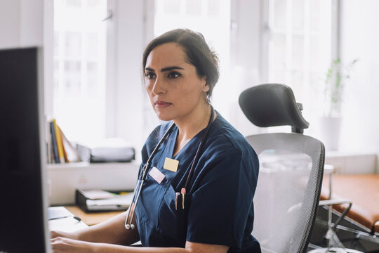 Focused female nurse working while sitting on chair in clinic