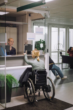 Female patient sitting on wheelchair and doing inquiry with receptionist at healthcare center