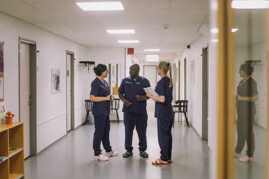 Male and female medical staff discussing together while standing in corridor at hospital