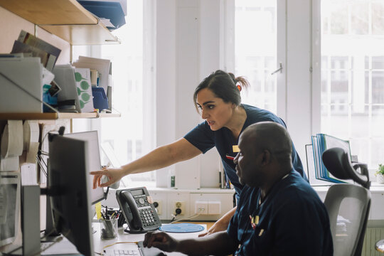 Female nurse pointing over computer while discussing with colleague at hospital