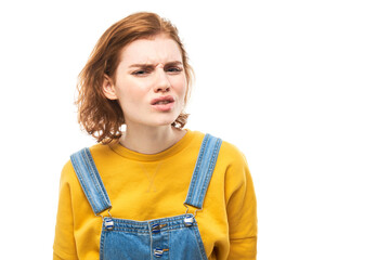 Portrait of young redhead woman in yellow casual suspiciously looking at camera isolated on white...