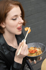 Beautiful young woman tastes udon noodles with shrimp and fried vegetables