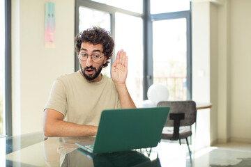 young adult bearded man with a laptop looking serious and curious, listening, trying to hear a secret conversation or gossip, eavesdropping