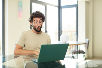 young adult bearded man with a laptop pressing lips together with a cute, fun, happy, lovely expression, sending a kiss