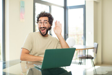 young adult bearded man with a laptop looking happy, listening, trying to hear a secret conversation or gossip, eavesdropping