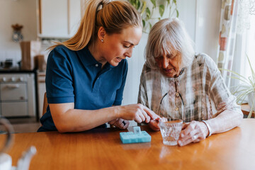 Female caregiver assisting senior woman while taking medicines at home