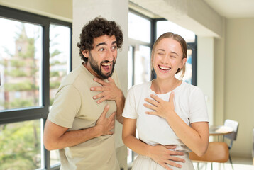 young adult couple laughing out loud at some hilarious joke, feeling happy and cheerful, having fun