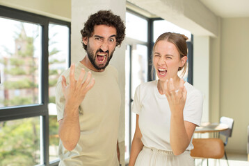 young adult couple looking angry, annoyed and frustrated screaming wtf or what’s wrong with you