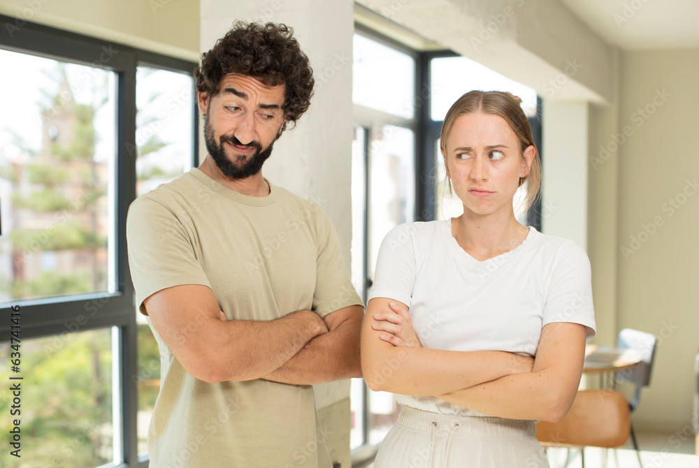 Wall mural young adult couple feeling displeased and disappointed, looking serious, annoyed and angry with crossed arms