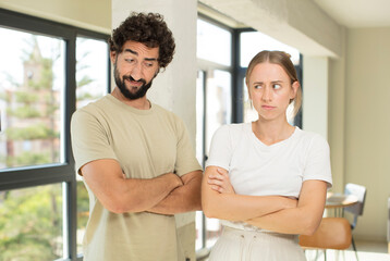 young adult couple feeling displeased and disappointed, looking serious, annoyed and angry with crossed arms