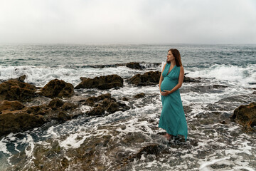 Pregnant woman posing in the long dress at Andalusian coast next to the sea